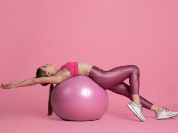 Flexible. Beautiful young female athlete practicing in studio, monochrome pink portrait. Sportive fit caucasian model training with fitball. Body building, healthy lifestyle, beauty and action concept.