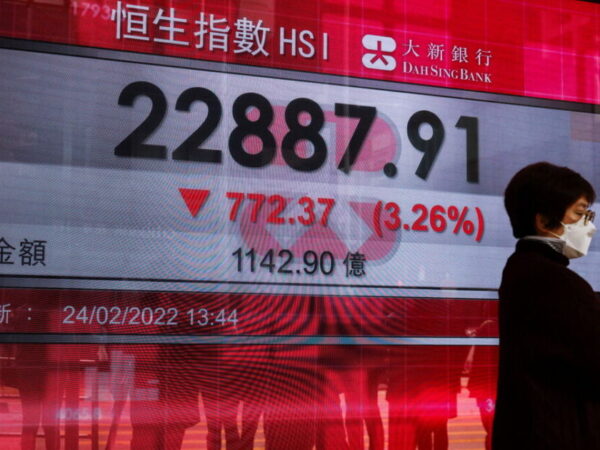 A woman wearing a face mask walks past a screen displaying Hang Seng Index, in Hong Kong, China February 24, 2022. REUTERS/Tyrone Siu