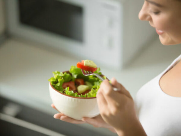 Bowl of fresh green salad hold in female hands, close up. Weight loss concept